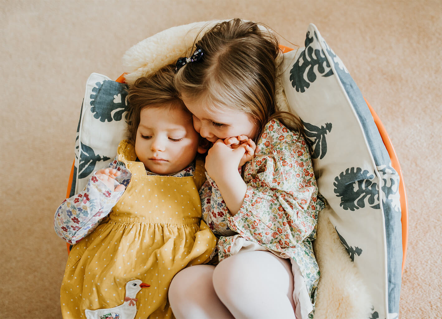 Emmy and her sister cuddling in a small craddle chair on cushions
